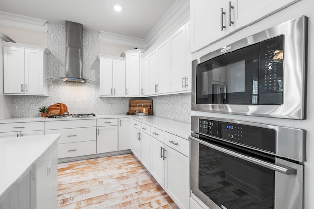 kitchen with tasteful backsplash, wall chimney exhaust hood, appliances with stainless steel finishes, light countertops, and crown molding