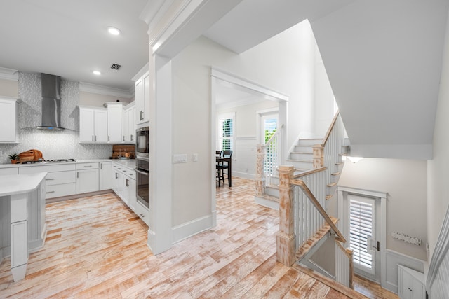 kitchen featuring visible vents, light wood-style flooring, ornamental molding, light countertops, and wall chimney range hood