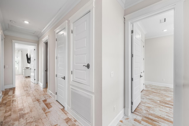 hall featuring visible vents, baseboards, light wood-type flooring, attic access, and crown molding