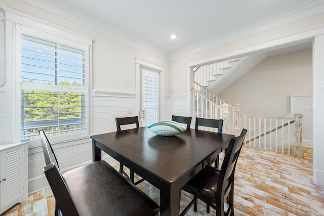 dining space with light wood-style floors, a wainscoted wall, ornamental molding, and stairs