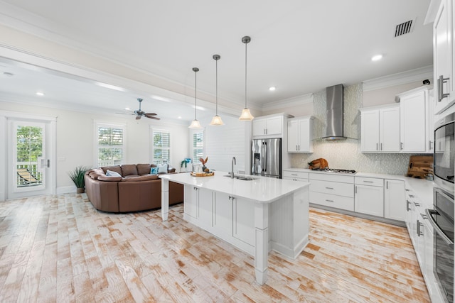 kitchen featuring visible vents, open floor plan, ornamental molding, appliances with stainless steel finishes, and wall chimney range hood