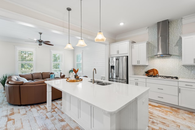 kitchen with wall chimney range hood, ornamental molding, stainless steel appliances, and a sink