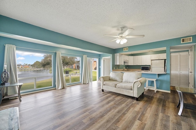 living room featuring ceiling fan, a textured ceiling, wood finished floors, and visible vents