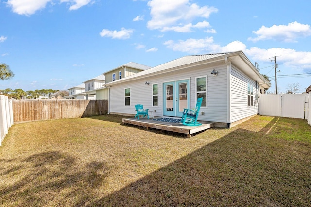 rear view of property with a deck, metal roof, a fenced backyard, french doors, and a lawn