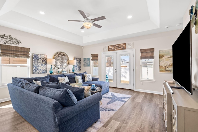 living room featuring light wood-type flooring, a raised ceiling, baseboards, and french doors