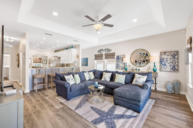 living area featuring light wood-type flooring, baseboards, visible vents, and a raised ceiling