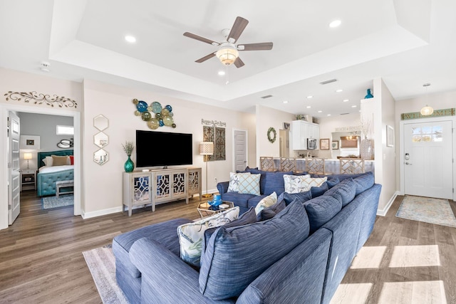 living room featuring wood finished floors, recessed lighting, a raised ceiling, and baseboards