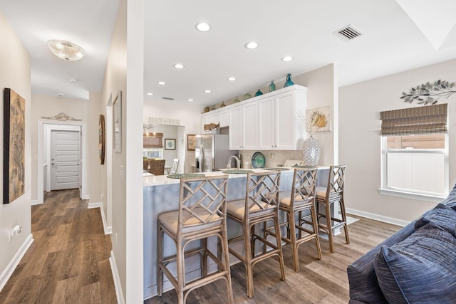 kitchen with wood finished floors, white cabinetry, a kitchen breakfast bar, stainless steel fridge with ice dispenser, and tasteful backsplash