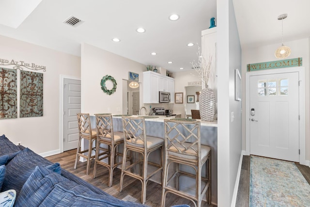 kitchen featuring stainless steel appliances, dark wood-style flooring, white cabinetry, decorative backsplash, and a kitchen bar