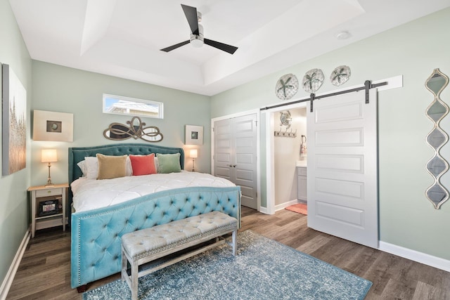 bedroom with a tray ceiling, a barn door, wood finished floors, and baseboards