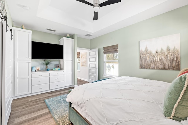 bedroom with a ceiling fan, a raised ceiling, visible vents, and light wood finished floors