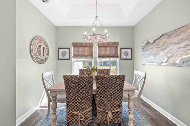 dining area with an inviting chandelier, baseboards, a raised ceiling, and dark wood-style flooring