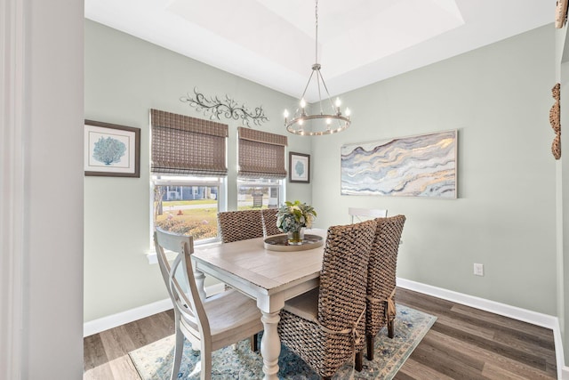 dining area with a notable chandelier, baseboards, a raised ceiling, and wood finished floors