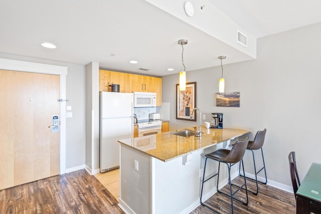 kitchen with visible vents, a kitchen bar, a peninsula, white appliances, and a sink