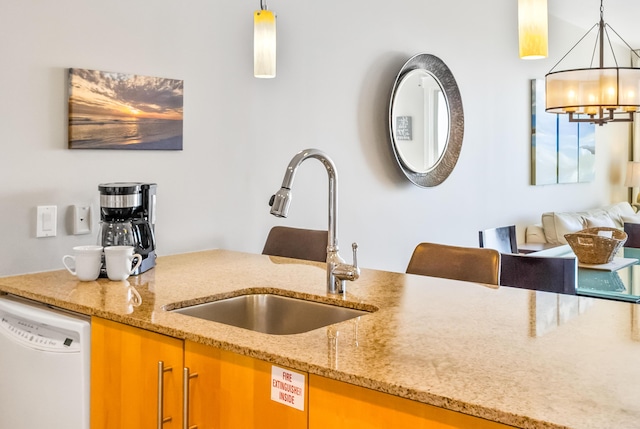 kitchen featuring dishwasher, decorative light fixtures, light stone counters, and a sink