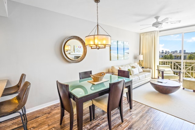 dining area with baseboards, wood finished floors, a view of city, and ceiling fan with notable chandelier