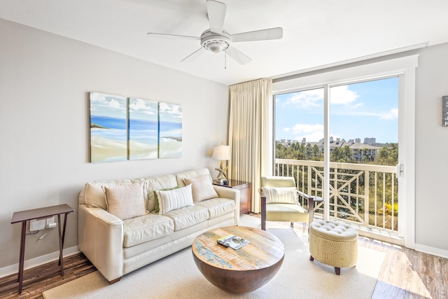 living area with a city view, wood finished floors, baseboards, and ceiling fan