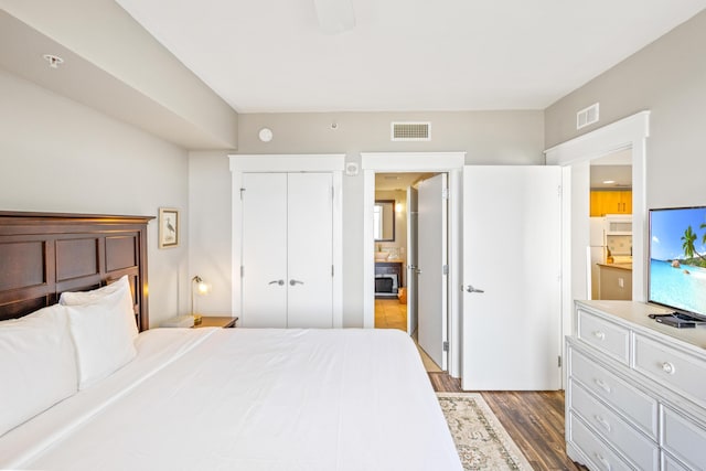 bedroom with dark wood-type flooring, freestanding refrigerator, visible vents, and a closet