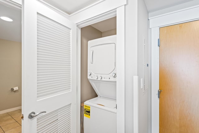 laundry area featuring light tile patterned floors, stacked washer / dryer, laundry area, and baseboards