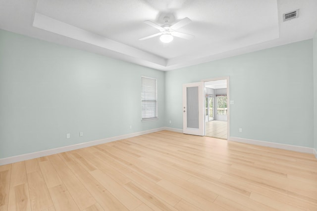 spare room with light wood finished floors, a raised ceiling, visible vents, and baseboards