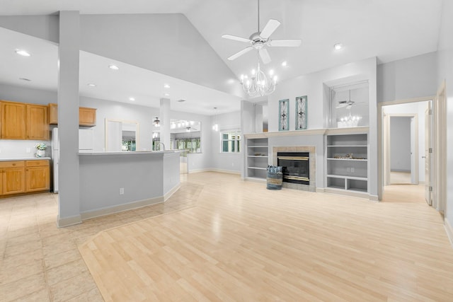 unfurnished living room featuring high vaulted ceiling, light wood-style flooring, a tiled fireplace, and ceiling fan with notable chandelier