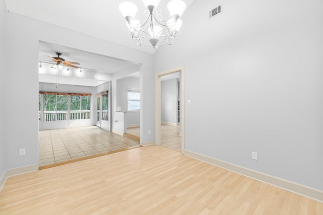 empty room featuring lofted ceiling, ceiling fan with notable chandelier, wood finished floors, visible vents, and baseboards