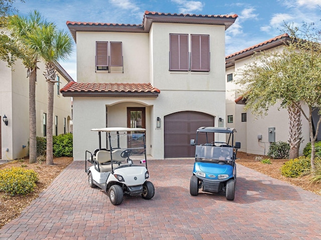 mediterranean / spanish-style house with a garage, decorative driveway, a tile roof, and stucco siding