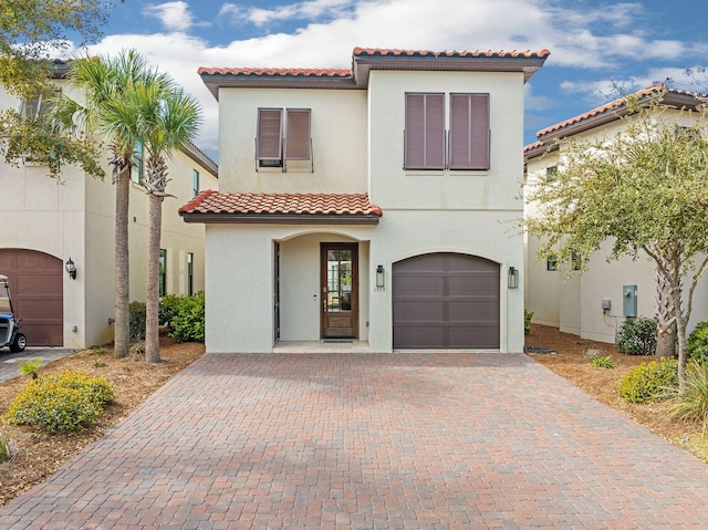 mediterranean / spanish-style house with a garage, decorative driveway, a tiled roof, and stucco siding