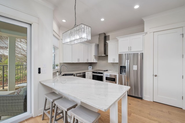 kitchen featuring tasteful backsplash, wall chimney exhaust hood, a peninsula, stainless steel appliances, and a sink