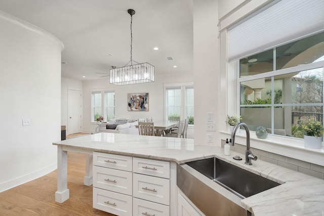 kitchen with light stone counters, light wood-style flooring, open floor plan, white cabinets, and a sink