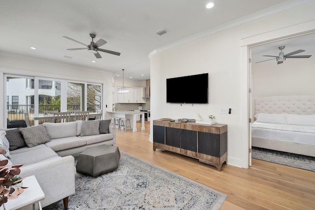 living area with a ceiling fan, visible vents, ornamental molding, and light wood-style flooring