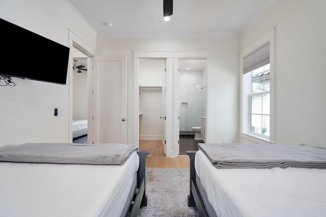 bedroom with a walk in closet, a closet, ensuite bathroom, ornamental molding, and light wood-type flooring