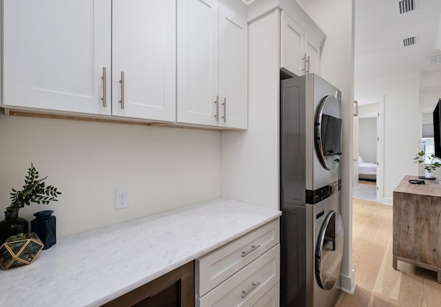 washroom with visible vents, stacked washer and dryer, light wood finished floors, and cabinet space