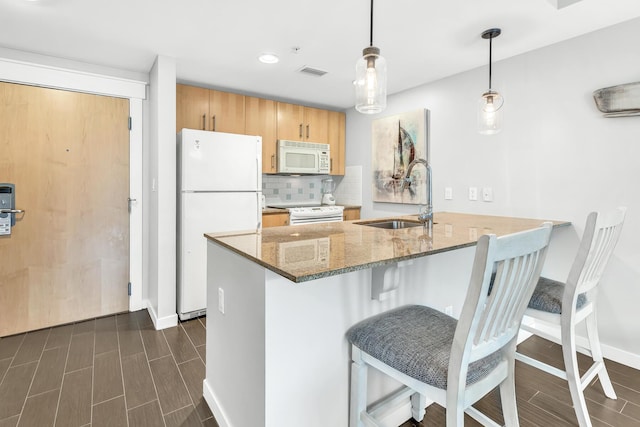 kitchen featuring a peninsula, white appliances, a sink, visible vents, and wood tiled floor