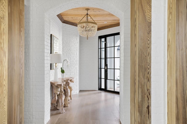 interior space featuring arched walkways, brick wall, wood finished floors, an inviting chandelier, and crown molding