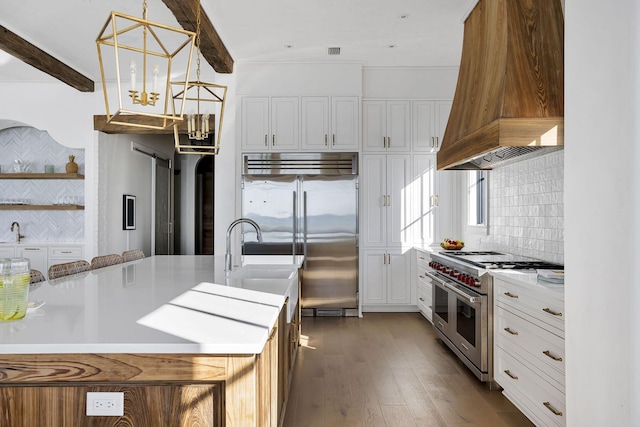 kitchen featuring beam ceiling, high end appliances, tasteful backsplash, light countertops, and premium range hood