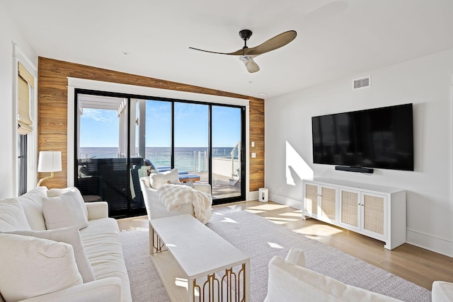 living room with wooden walls, baseboards, visible vents, ceiling fan, and wood finished floors