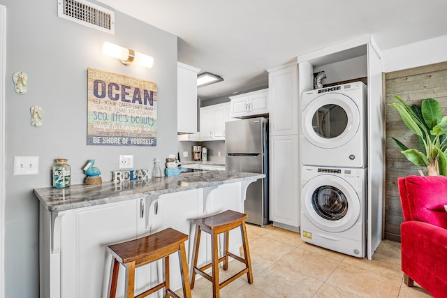 kitchen featuring a breakfast bar area, light tile patterned floors, visible vents, freestanding refrigerator, and stacked washing maching and dryer