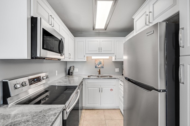 kitchen featuring light stone counters, light tile patterned flooring, a sink, white cabinets, and appliances with stainless steel finishes