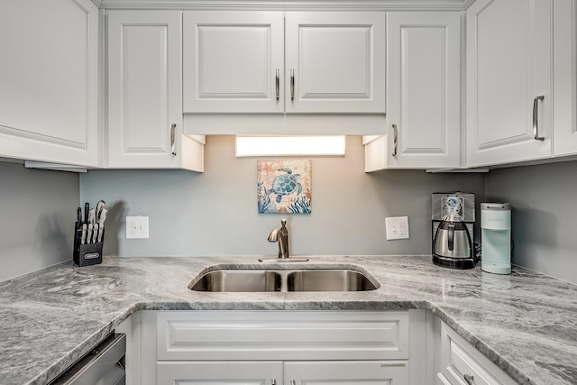 kitchen with light stone countertops, stainless steel dishwasher, white cabinets, and a sink