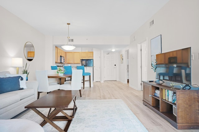 living room featuring visible vents, light wood-style flooring, and baseboards