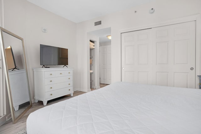 bedroom with a closet, wood finished floors, visible vents, and baseboards