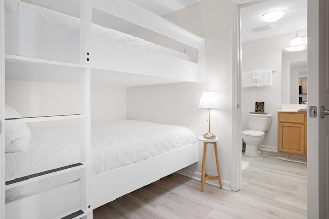 bedroom featuring baseboards, visible vents, light wood finished floors, and ensuite bathroom