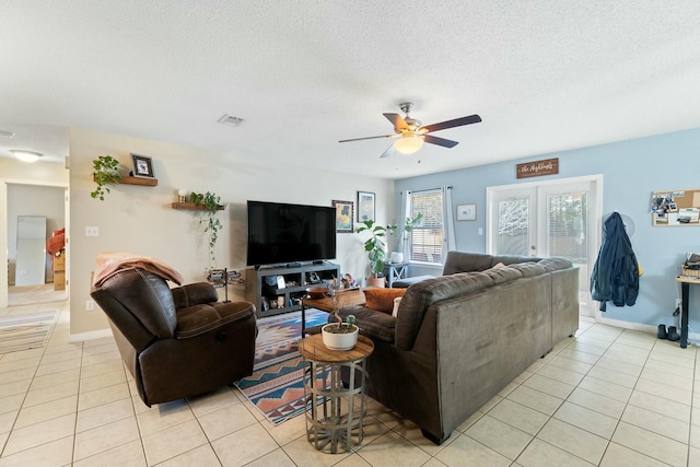 living room featuring visible vents, a textured ceiling, light tile patterned flooring, baseboards, and ceiling fan