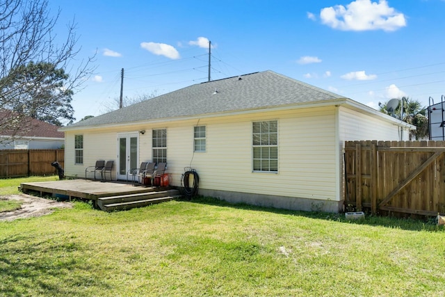 rear view of house featuring a lawn, a deck, a fenced backyard, french doors, and a shingled roof