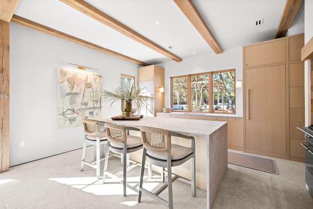 kitchen with light stone countertops, a center island, a breakfast bar area, light brown cabinets, and beam ceiling