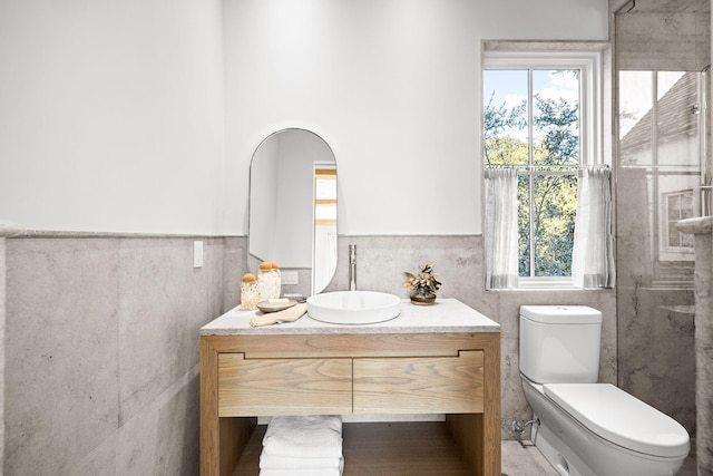 bathroom with toilet, vanity, a wainscoted wall, and tile walls