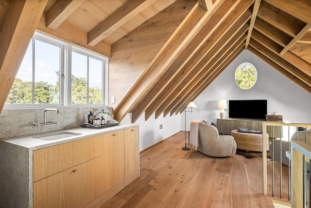 additional living space featuring vaulted ceiling with beams, light wood-type flooring, and a sink