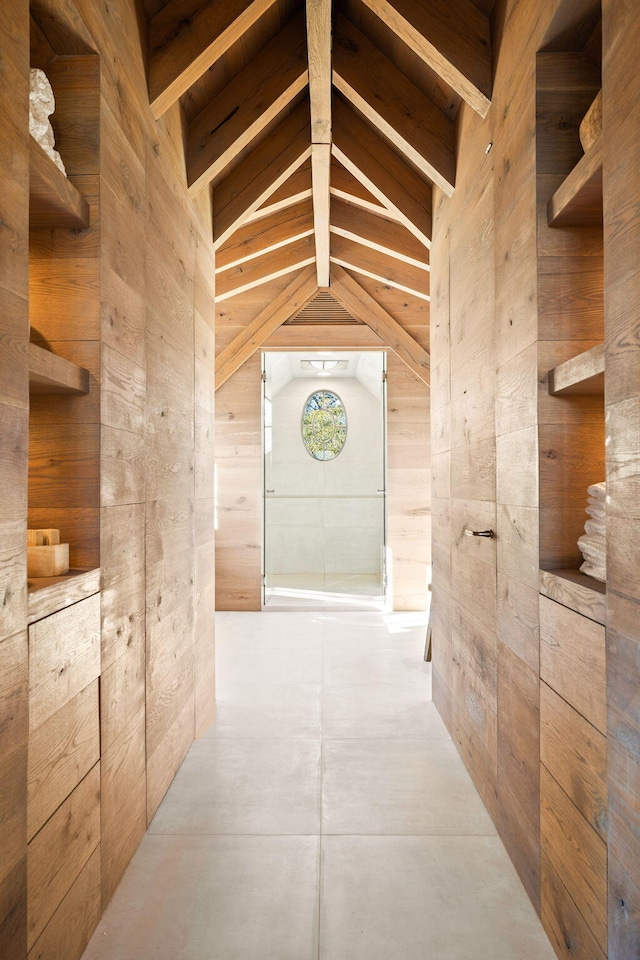 corridor with wood walls, concrete floors, and lofted ceiling with beams