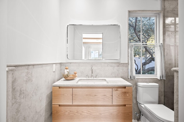 bathroom with vanity, tile walls, toilet, and wainscoting